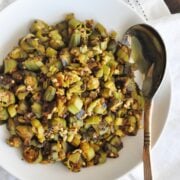 A white plate showcases a vibrant serving of Bhindi Fry, with sautéed okra pieces perfectly mixed with aromatic spices. A metal spoon rests invitingly on the plate, placed on a pristine white cloth, ready to serve.