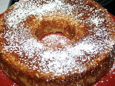A round, brown bundt cake reminiscent of Ina Gartens sour cream coffee cake, dusted lovingly with powdered sugar on top.