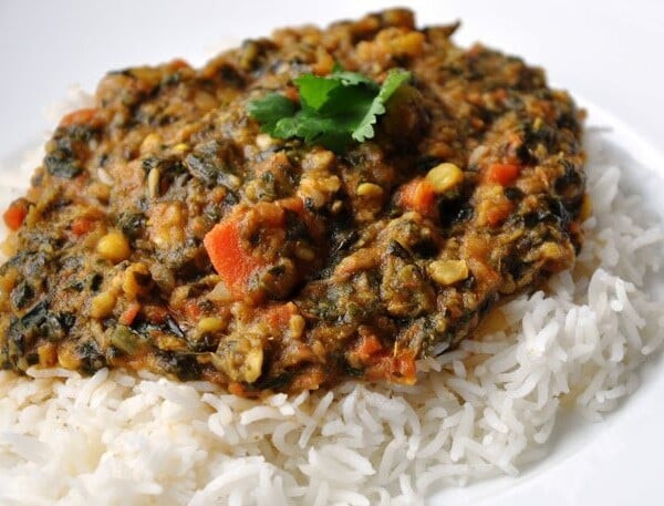 A serving of rice topped with sai bhaji, a delightful mixed vegetable curry, garnished with a sprig of cilantro.