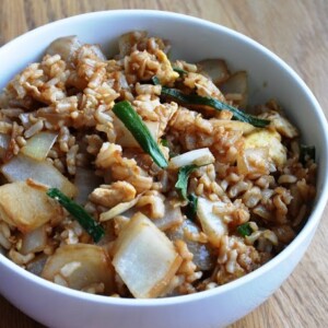 A bowl of quick and easy egg fried rice with onions, green onions, and scrambled eggs rests invitingly on a wooden table.