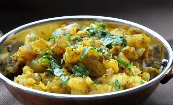 A bowl of spiced potato curry garnished with fresh cilantro, served in a metal dish.