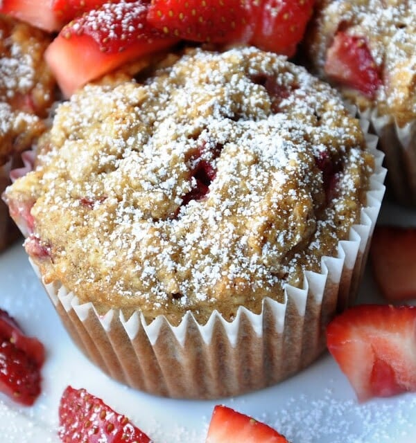 Strawberry muffin topped with powdered sugar, surrounded by fresh strawberry slices.