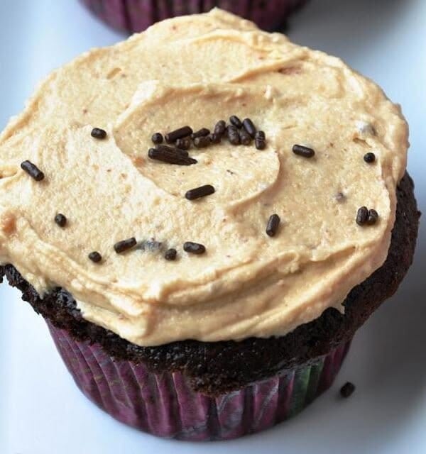 Chocolate cupcake with peanut butter frosting, topped with chocolate sprinkles, on a white surface.