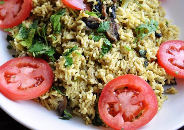 A plate of Mushroom Matar Pulao, featuring spiced rice and tender mushrooms, garnished with fresh cilantro and tomato slices.