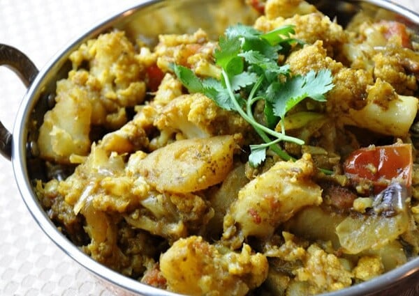 A metal bowl filled with a potato and cauliflower curry garnished with fresh cilantro.