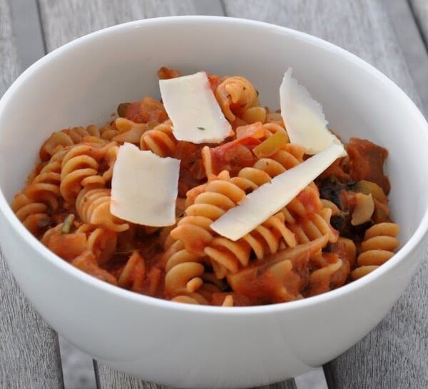A white bowl of rotini pasta in tomato sauce topped with three slices of cheese on a wooden table.