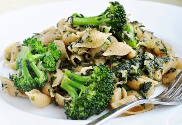 A plate of shell pasta with broccoli and spinach, served with a fork on a white plate.