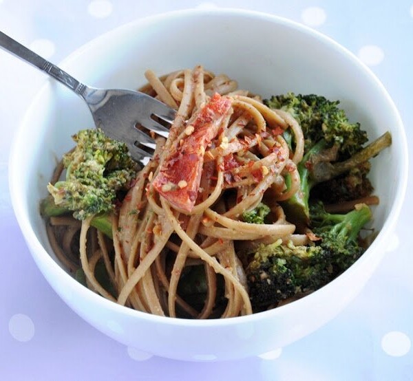 A bowl of spaghetti with broccoli, tomato pieces, and red pepper flakes, with a fork in the dish.
