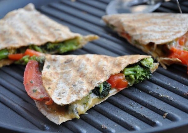 Three vegetable quesadillas with tomatoes, broccoli, and melted cheese on a grill pan.