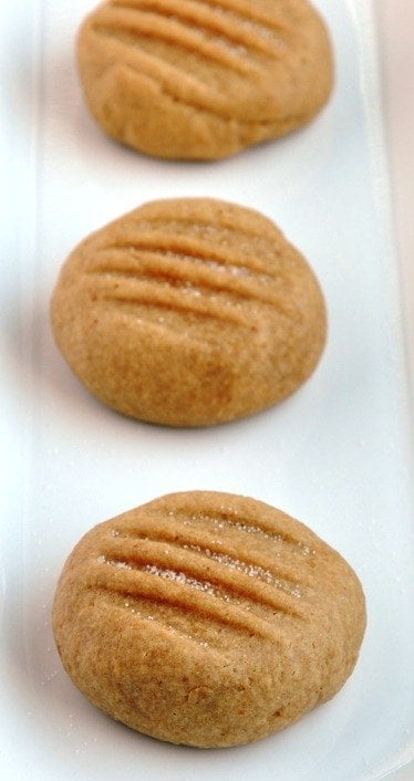 Three round, lightly browned vegan soft peanut butter cookies with fork indents rest on a white rectangular plate.