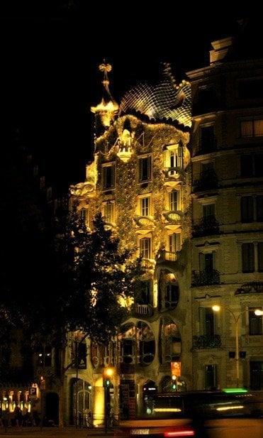 An ornate building with elaborate architecture is illuminated at night, capturing the enchanting allure of Barcelona, Spain.
