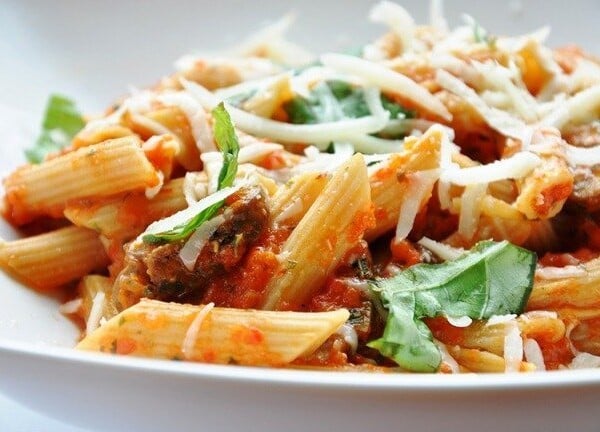 Close-up of a plate of penne pasta with tomato sauce, garnished with melted cheese and fresh basil leaves.