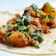 A tortilla topped with a vibrant sautéed vegetable and herb medley, reminiscent of an aloo masala kati roll.
