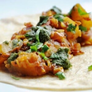 A tortilla topped with a vibrant sautéed vegetable and herb medley, reminiscent of an aloo masala kati roll.