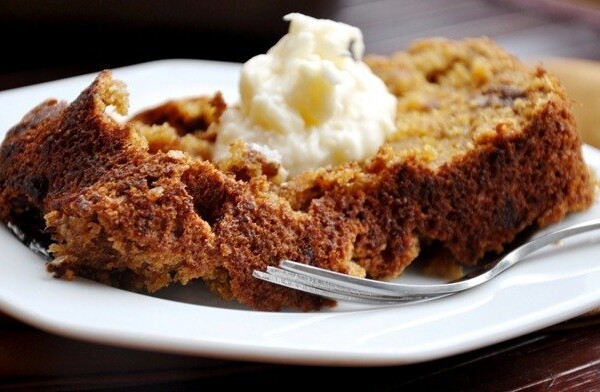 A slice of moist cake with a dollop of whipped cream on top, served on a white plate with a fork.