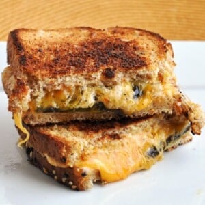 Indulge in a Jalapeno Popper Grilled Cheese Sandwich, where every bite reveals gooey melted cheese and spicy jalapeños. Stacked on a white plate, the top piece is enticingly half-eaten, inviting you to savor its deliciousness.
