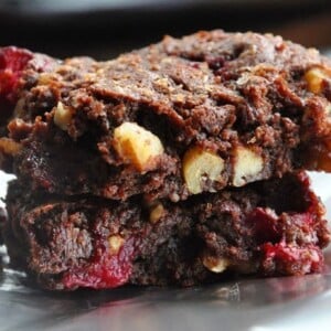 Two stacked chocolate cranberry walnut cookies rest on a shiny surface, reminiscent of fudgy cranberry walnut brownies.