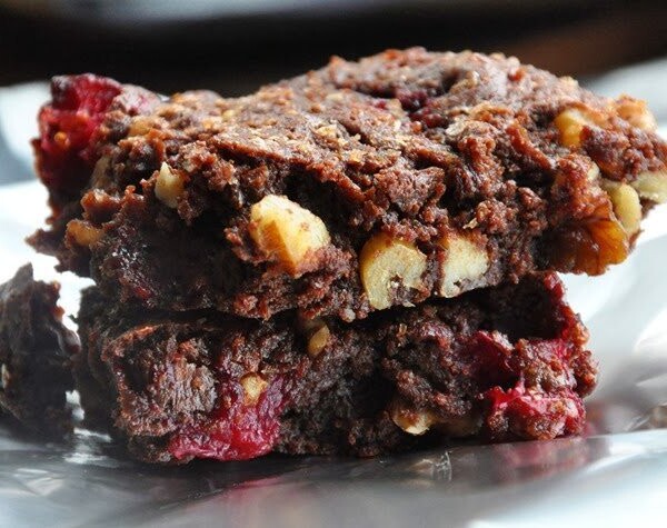 Two stacked chocolate cranberry walnut cookies rest on a shiny surface, reminiscent of fudgy cranberry walnut brownies.