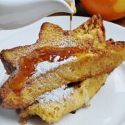 Pandora French toast topped with powdered sugar sits on a white plate, while golden syrup cascades over it.