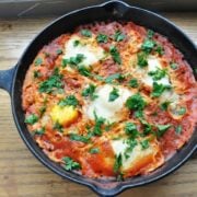 A cast iron skillet cradles a delightful shakshuka: poached eggs nestled in a rich tomato and pepper sauce, all garnished with fresh chopped parsley.