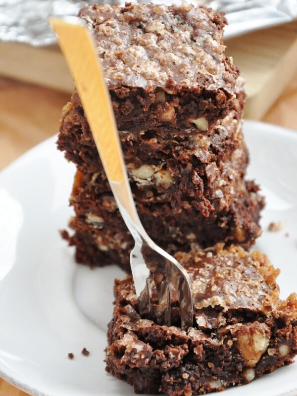 A stack of flourless chocolate walnut brownies sits enticingly on a white plate, with a fork playfully inserted into the top piece.