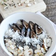 A bowl with sliced figs, shredded coconut, chia seeds, and almond slices is complemented by cardamom pods on a cutting board nearby—an enticing blend reminiscent of cardamom rosewater oatmeal that infuses your morning with aromatic spice.