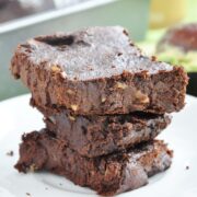 A stack of three rich, gooey flourless avocado brownies with crunchy walnuts sits enticingly on a white plate.