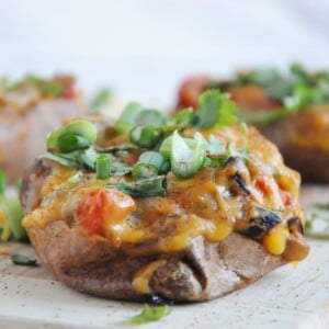 Stuffed mushrooms topped with melted cheese, chopped green onions, and cilantro rest invitingly on a wooden board, complemented perfectly by a side of chipotle black beans.