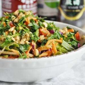 A salad in a white bowl featuring mixed greens, shredded carrots, and chopped nuts, complemented by refreshing zucchini noodles. Touches of herbs enhance the dish, while bottles of condiments quietly peek from the background.
