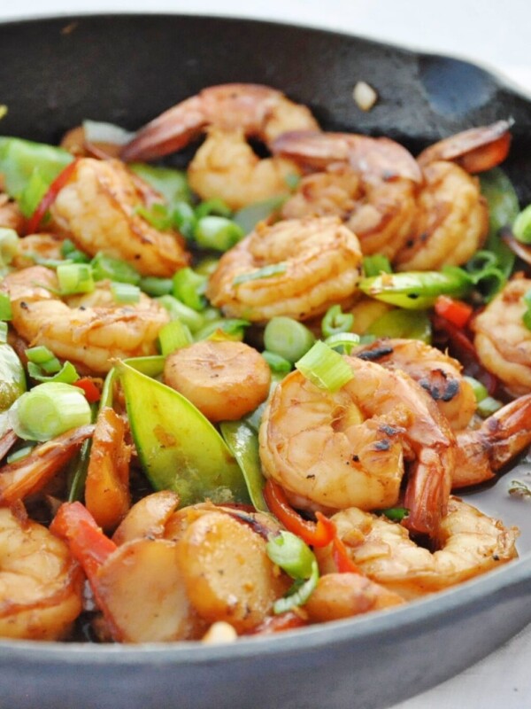 A skillet brimming with Chili Garlic Shrimp, snap peas, red bell peppers, and sliced green onions in a savory sauce.