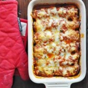Baked lasagna in a rectangular dish sits invitingly next to a red oven mitt on a wooden surface, while the comforting aroma of eggplant and spinach rollatini fills the air.