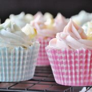Lemon cupcakes with pastel frosting and a lemon slice adorn a cooling rack, wrapped in checkered pastel blue and pink. The delightful lemon buttercream adds an extra zing to these charming treats.