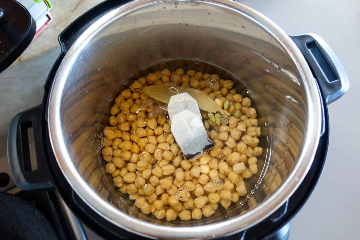 Uncooked chickpeas, bay leaf, and 2 tea bags in water inside an Instant Pot for making Punjabi Chole.