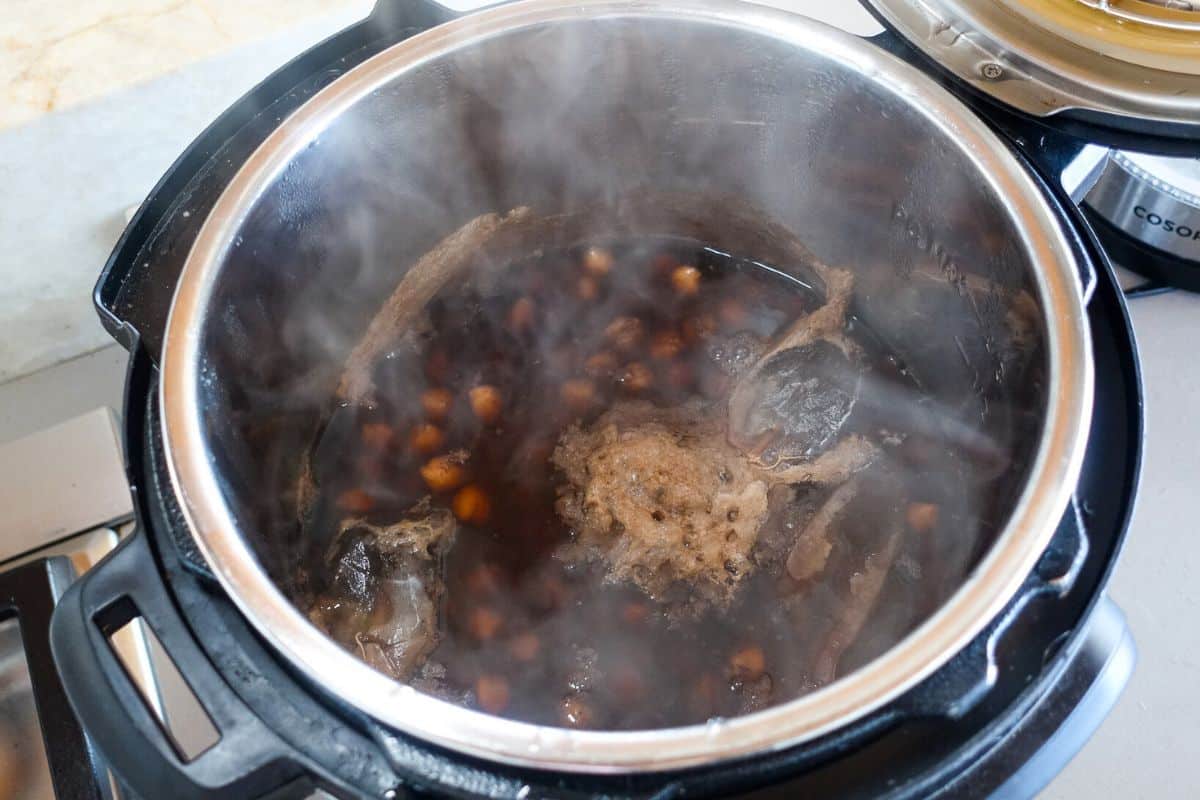 An Instant Pot with cooked chickpeas containing teabags nad spices for making Punjabi Chole.