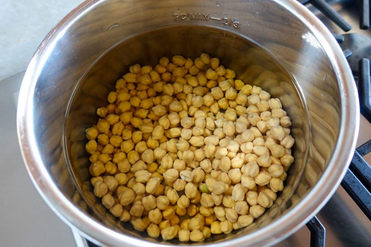 A stainless steel pot containing uncooked chickpeas with water sits on a stove.