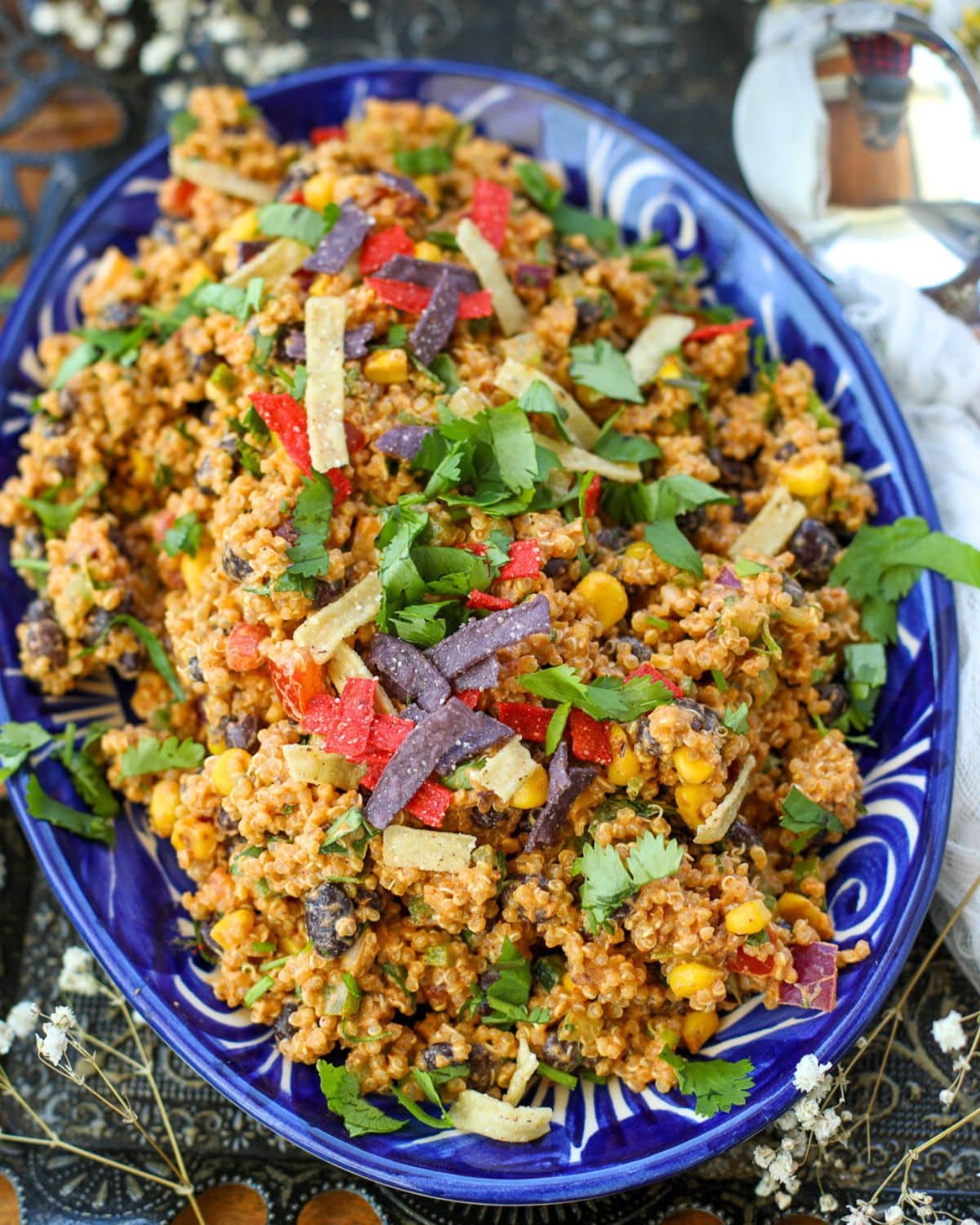 A blue oval dish filled with quinoa taco salad mixed with corn, black beans, cilantro, colorful tortilla strips, and chipotle aioli.