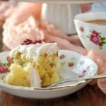 A slice of Rose Water Cake with Almonds & Rose Buttercream sits on a floral plate next to a cup of tea in a matching floral teacup.