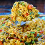 A large spoonful of tomato spinach orzo pasta with Indian spices.