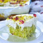 Pistachio Milk Cake topped with whipped cream, ground pistachios, and dried rose petals.