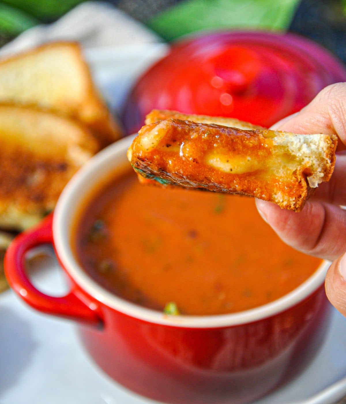 Grilled cheese sandwich being dipped in a bowl of tomato basil soup.