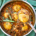 Egg Masala with boiled eggs in a serving dish topped with slit green chilies and fresh cilantro.