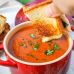 Grilled cheese sandwich being dipped in a bowl of tomato basil soup.