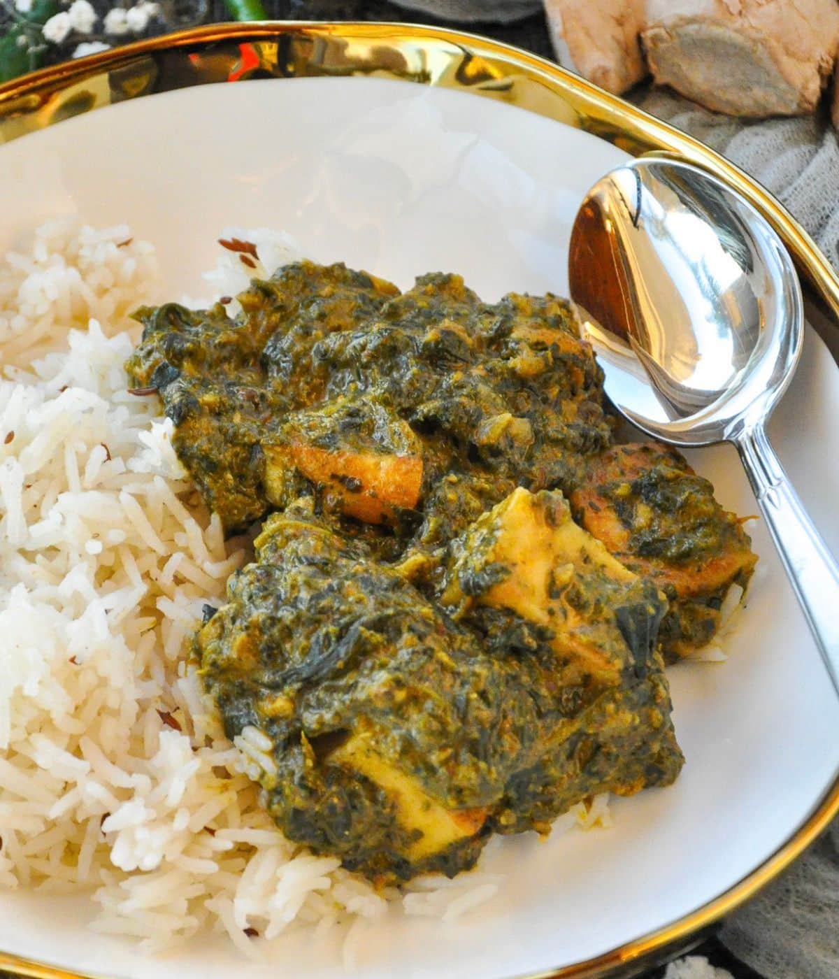 A white bowl consisting of jeera rice with palak paneer, and a silver spoon.