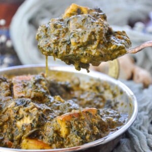 A white bowl consisting of jeera rice with palak paneer, and a silver spoon.