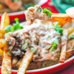 In N Out Animal Style Masala Fries with a fry being lifted over a bunch of fries and sauce in the background.