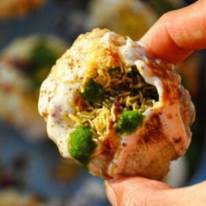 Holding up a dahi puri filled with potatoes, black chickpeas, yogurt, chutneys, spices, and sev.