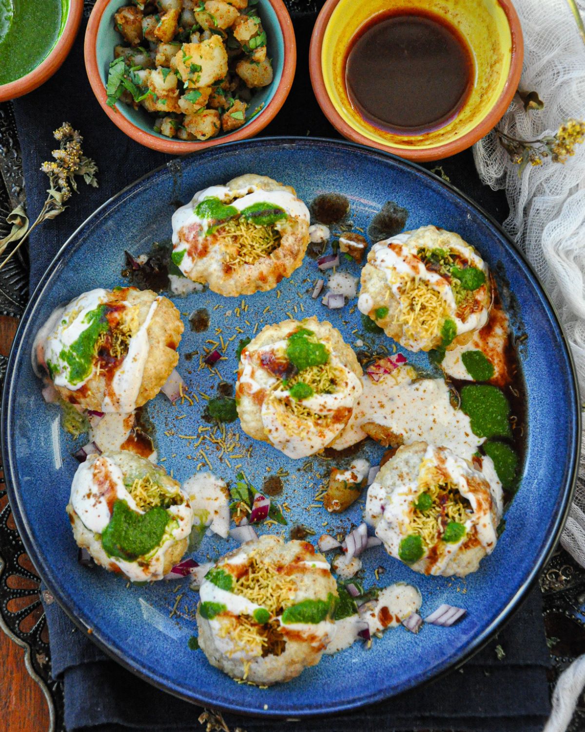 Dahi Puri consisting of potatoes, black chickpeas, yogurt, chutneys, and spices on a blue plate.