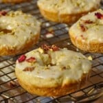 Ras Malai donuts sitting on a wire rack and topped with a saffron-cardamom glaze, chopped pistachios, and edible rose petals.