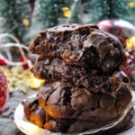 A stack of levain bakery dark chocolate chocolate chip cookies on a plate with a snow covered christmas tree in the back.