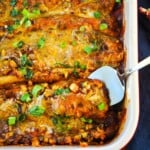 Bean and Cheese Enchiladas garnished with cilantro and scallions with a ladle slightly pulling out an enchilada.